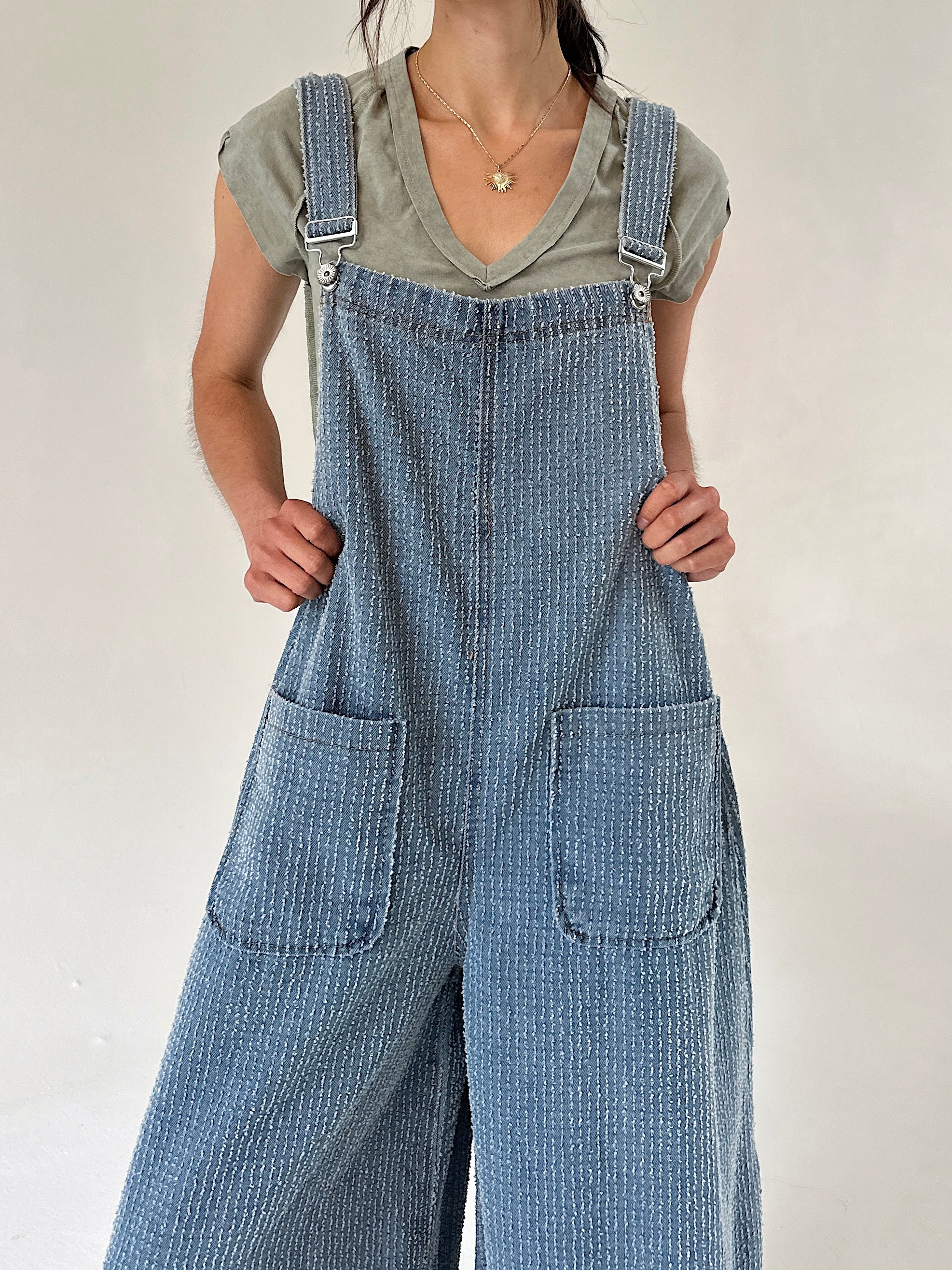 Person wearing blue denim textured overalls over a green t-shirt against a plain background