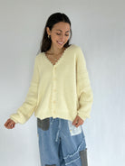 Woman wearing a light yellow cardigan and blue jeans against a white background