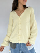 Person wearing a light yellow cardigan with lace trim on a plain background