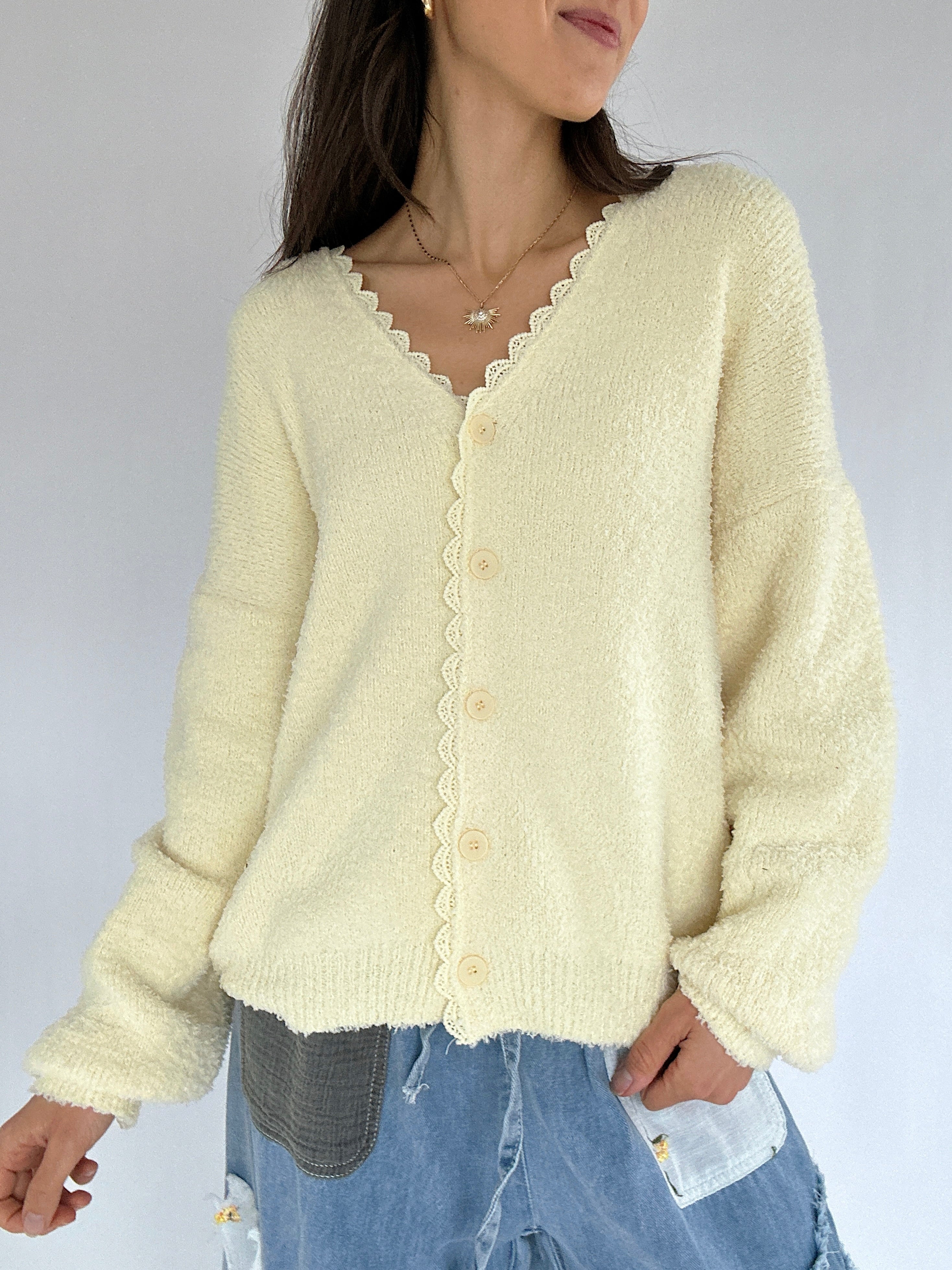 Person wearing a light yellow cardigan with lace trim on a plain background