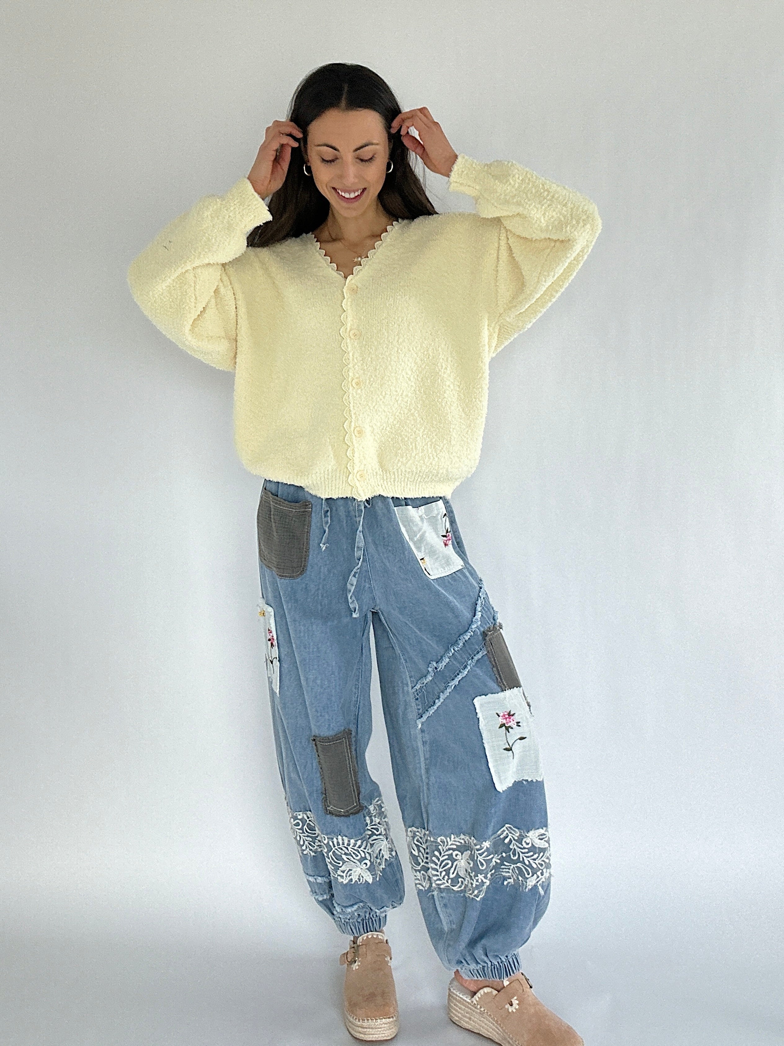 Woman wearing a light yellow cardigan and patchwork jeans on a white background