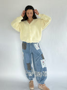 Woman wearing a light yellow cardigan and patchwork jeans on a white background