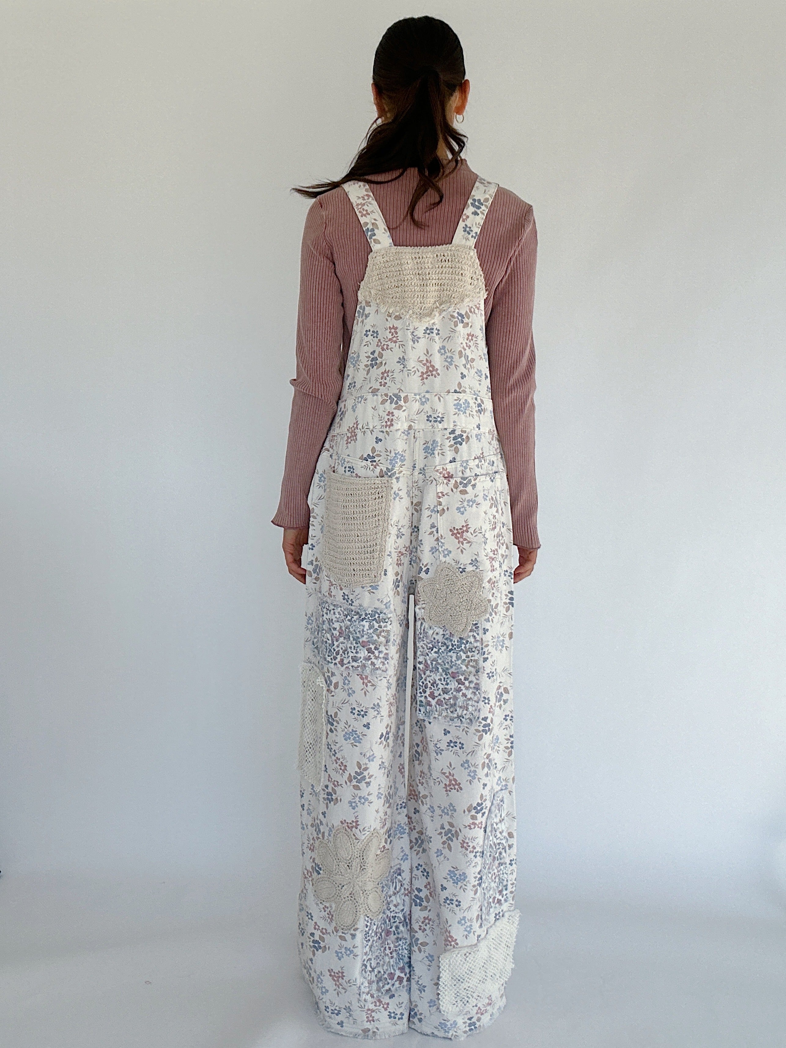 Person wearing a floral overalls with a plain background back view