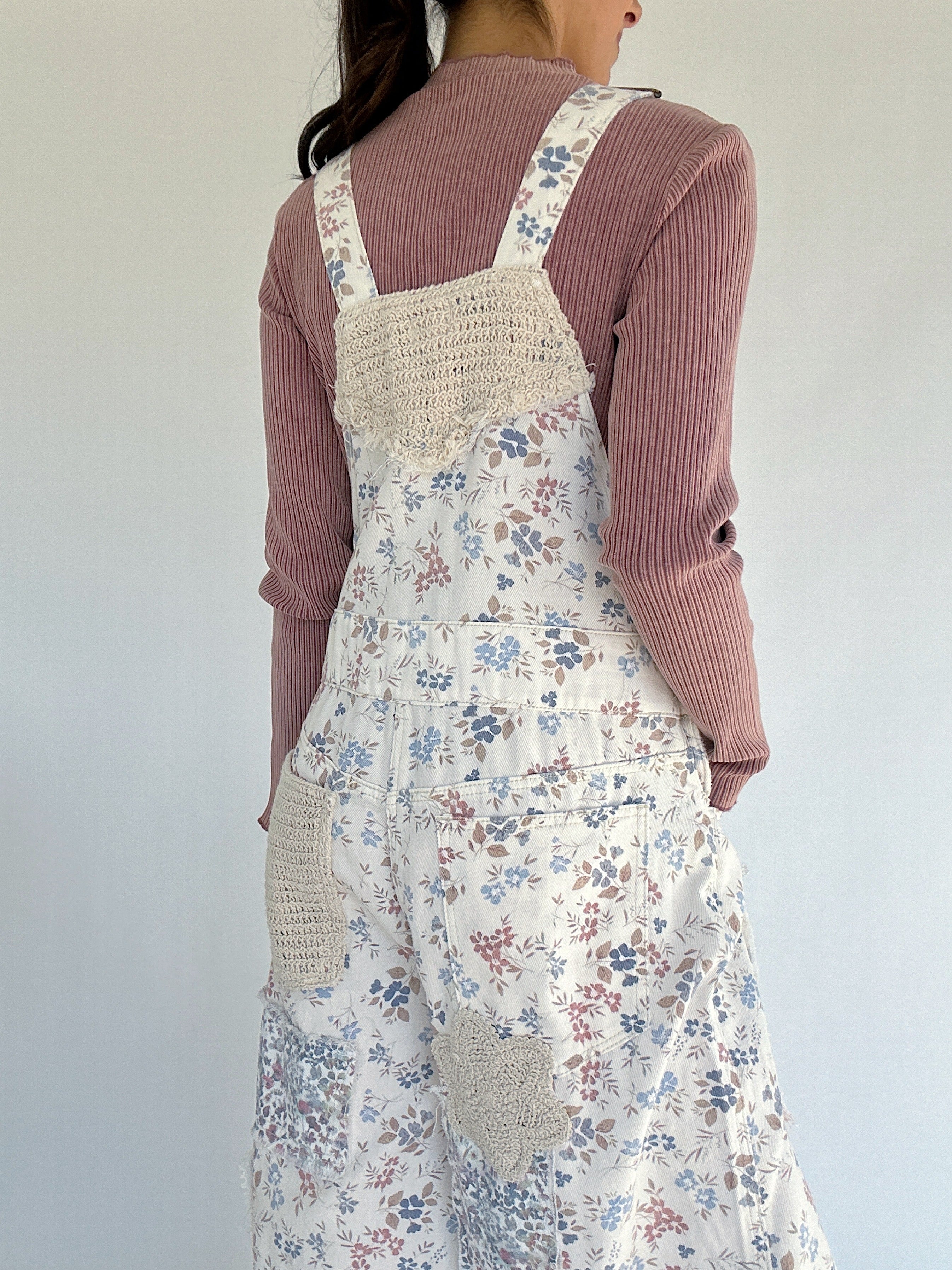 Person wearing floral overalls over a pink sweater against a white background