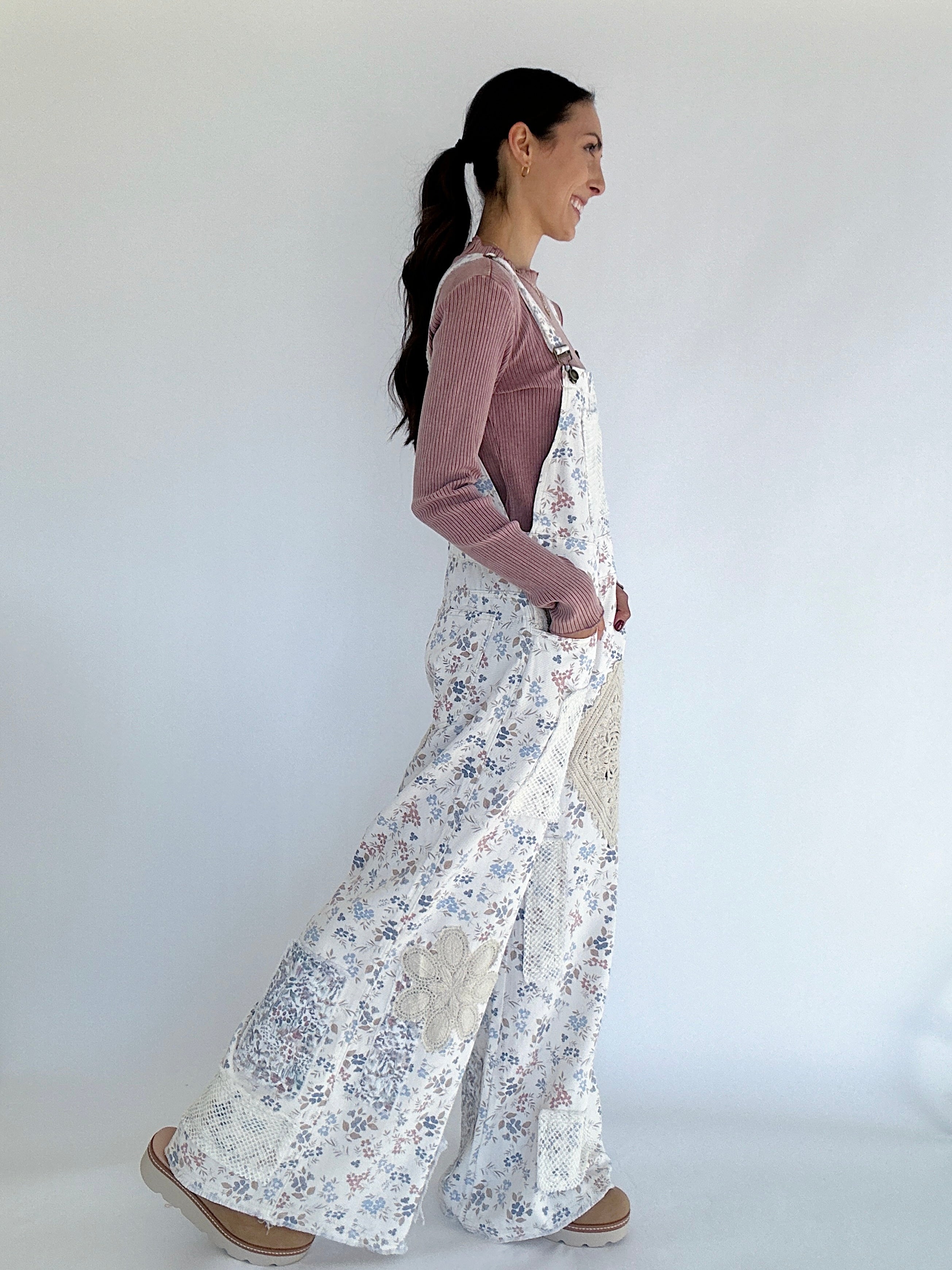 Woman wearing floral overalls and pink sweater against a white background side view