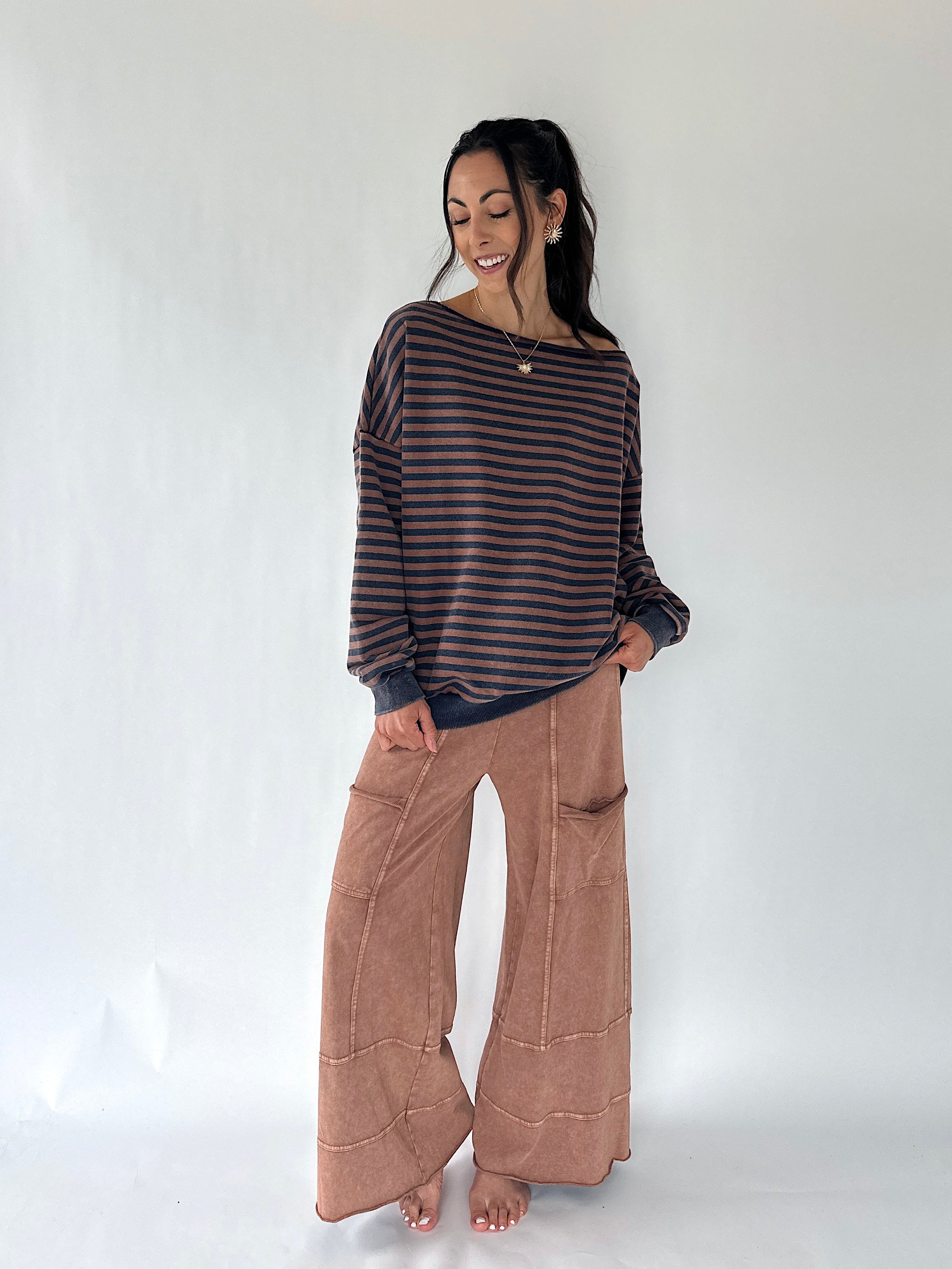 A woman modeling a dark brown and black striped long-sleeve knit top with wide-leg brown pants, standing against a plain white studio background.