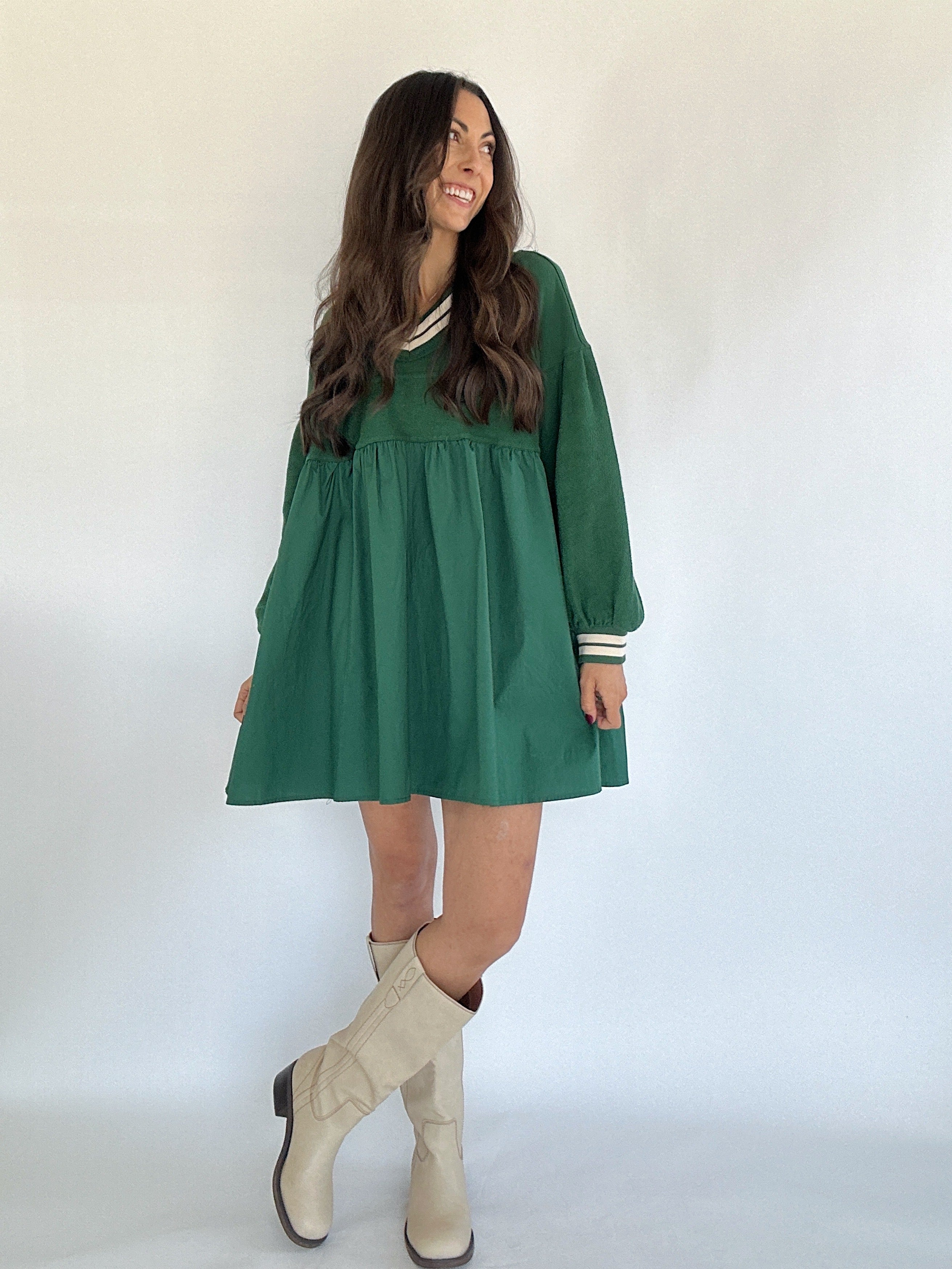 Woman wearing a green dress with long sleeves and beige knee-high boots on a white background