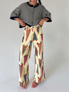 A woman modeling a two-piece outfit consisting of a blue and white striped short-sleeve cardigan and high-waisted, wide-leg pants featuring a vintage pennant flag print on a cream background.
