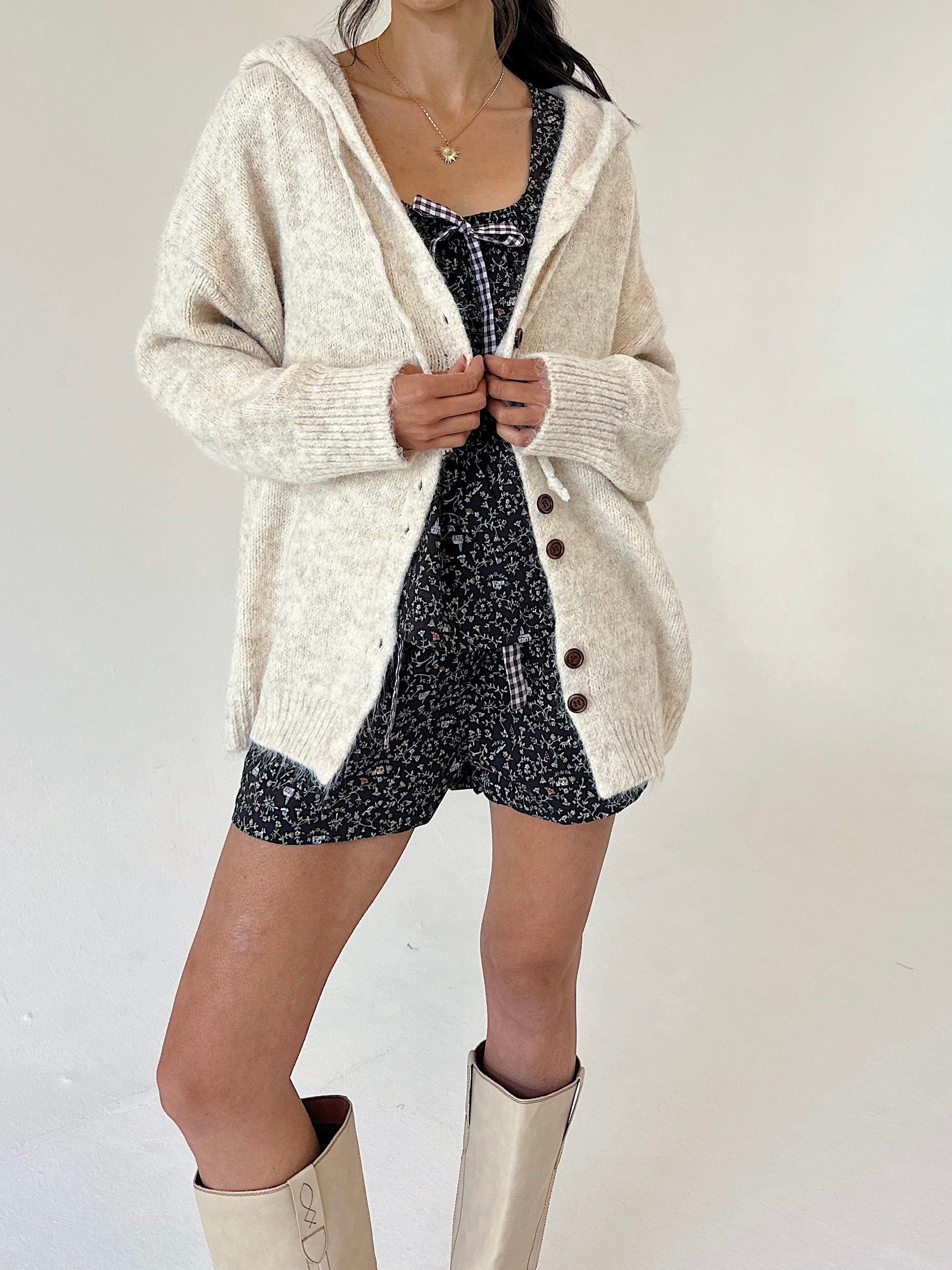 A model wearing a cream-colored, textured knit cardigan over a set, paired with beige boots, against a plain off-white background.
