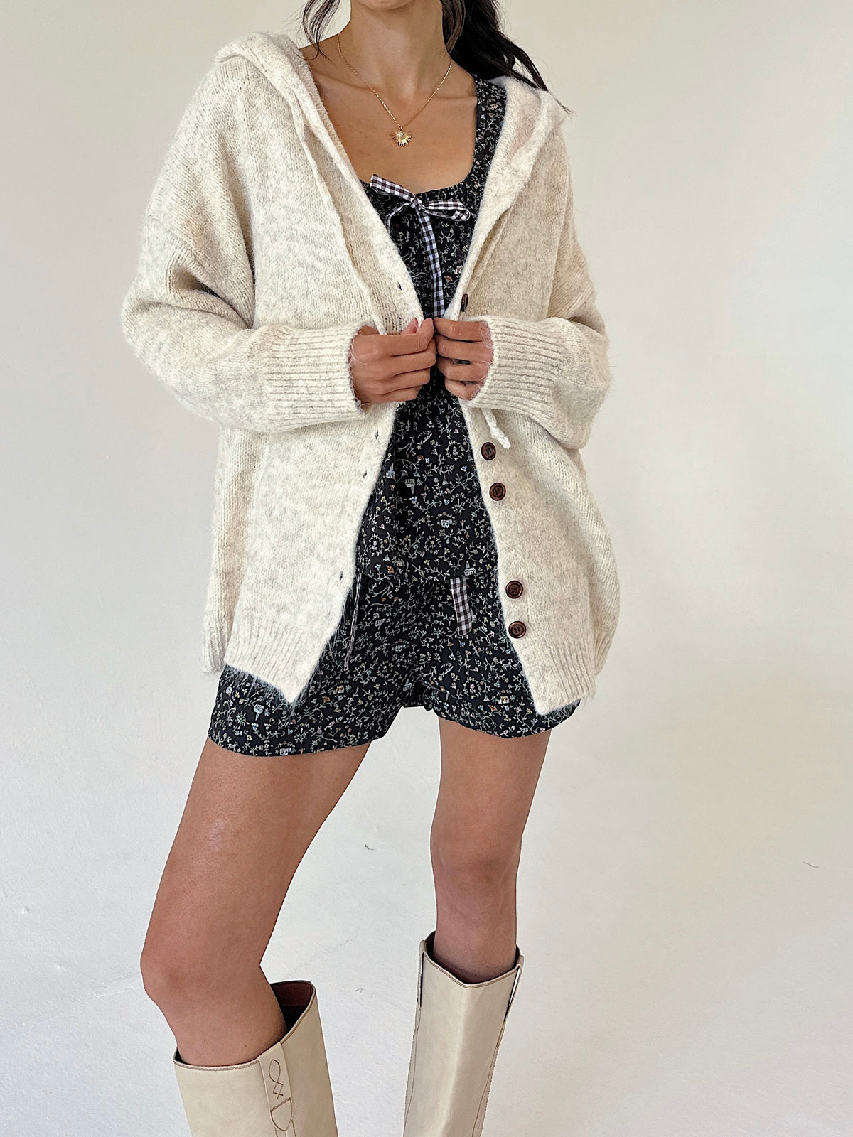 A model wearing a cream-colored, textured knit cardigan over a set, paired with beige boots, against a plain off-white background.