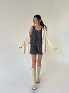 A woman modeling a matching two-piece lounge set with a black and white speckled pattern, styled with a cream-colored cardigan and cream-colored knee-high boots against a plain studio background.