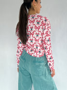 Person wearing a cardigan with red bow and candy cane pattern and teal pants against a plain background