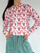 Person wearing a white shirt with red bow and candy cane pattern and green accents, paired with teal pants on a plain background.