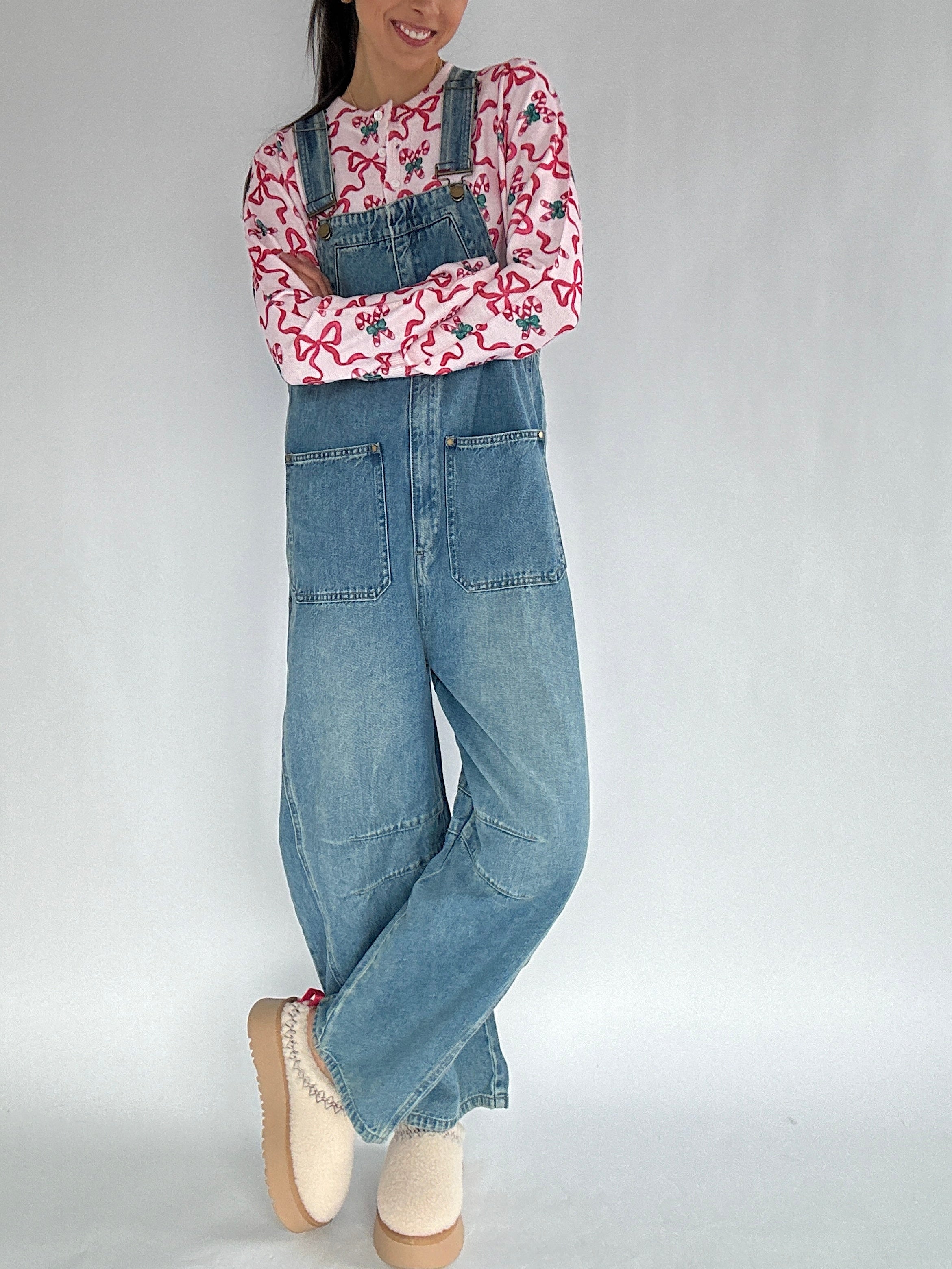 Person wearing a candy cane and bow patterned cardigan and denim overalls on a plain background