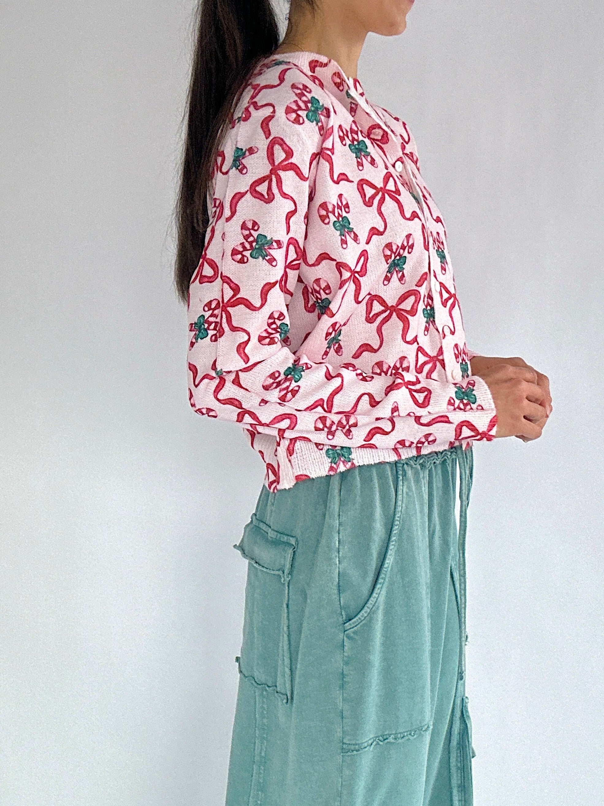 Person wearing a pink candy cane and bow-patterned cardigan from side with a white background