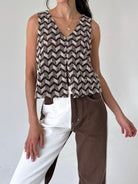 A woman wearing a sleeveless knit top with a brown and beige chevron pattern, styled with split-color pants against a plain light background.
