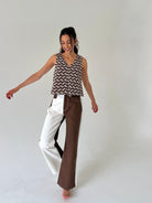 A woman modeling a sleeveless V-neck top with a brown and beige chevron pattern, paired with wide-leg pants split down the middle into white and brown sections, against a plain light gray studio background.