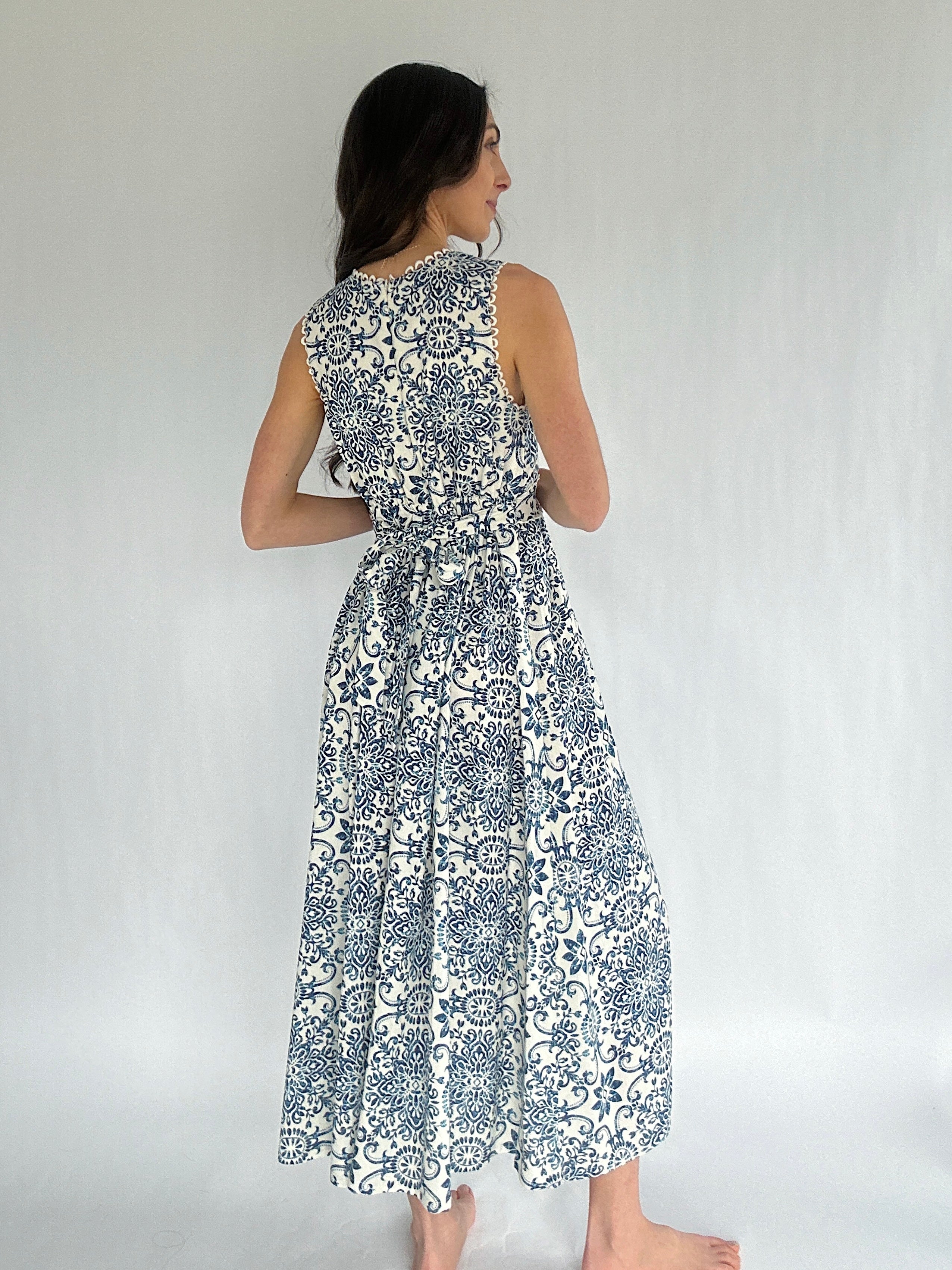 Woman wearing a sleeveless dress with a blue and white pattern on a plain background showing back zip and waist tie