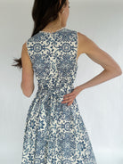 Woman wearing a blue and white patterned dress against a plain background showing back zipper and tie