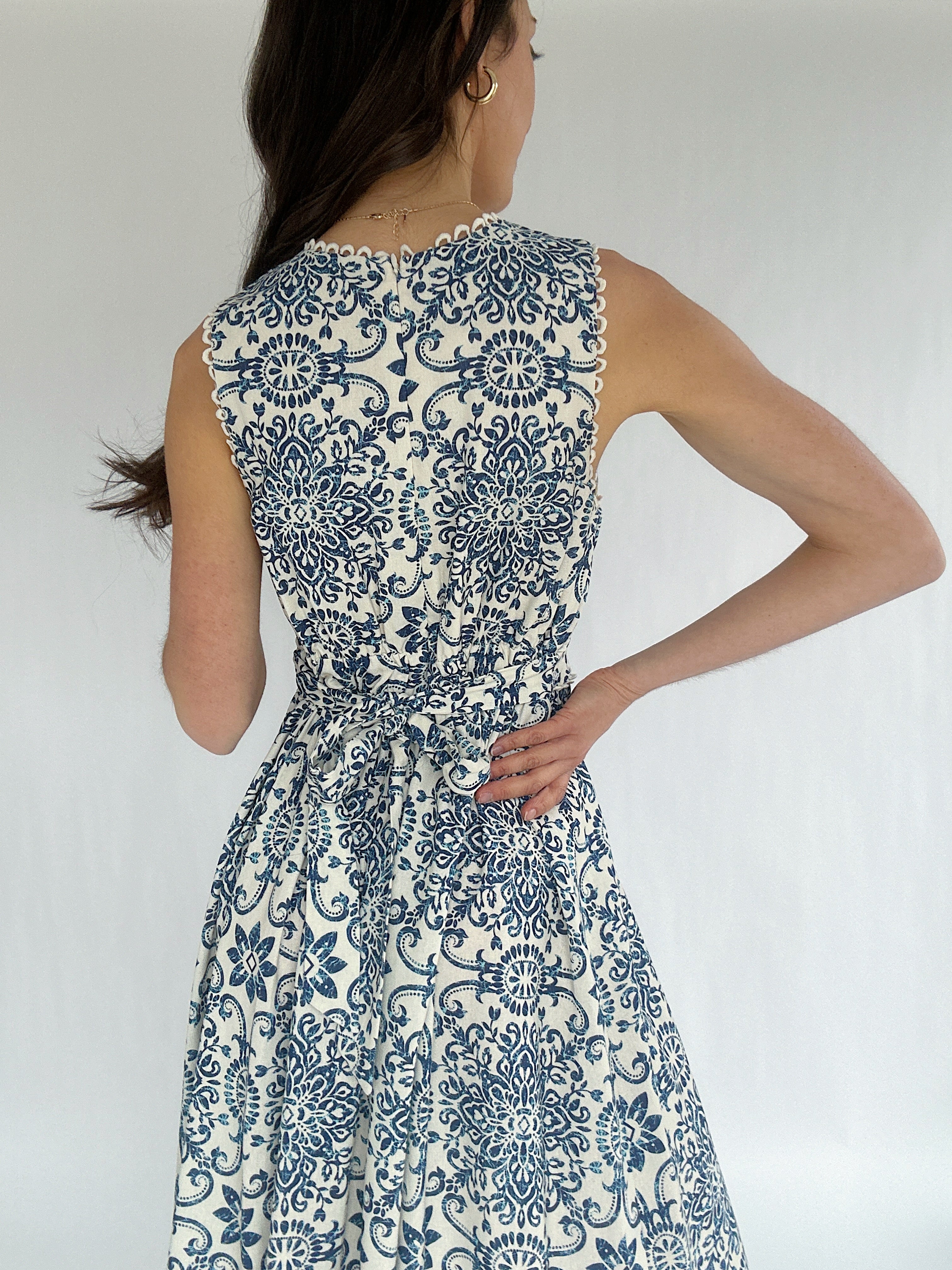 Woman wearing a blue and white patterned dress against a plain background showing back zipper and tie