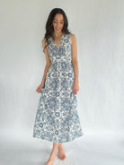 Woman wearing a sleeveless dress with a white and blue pattern against a plain background