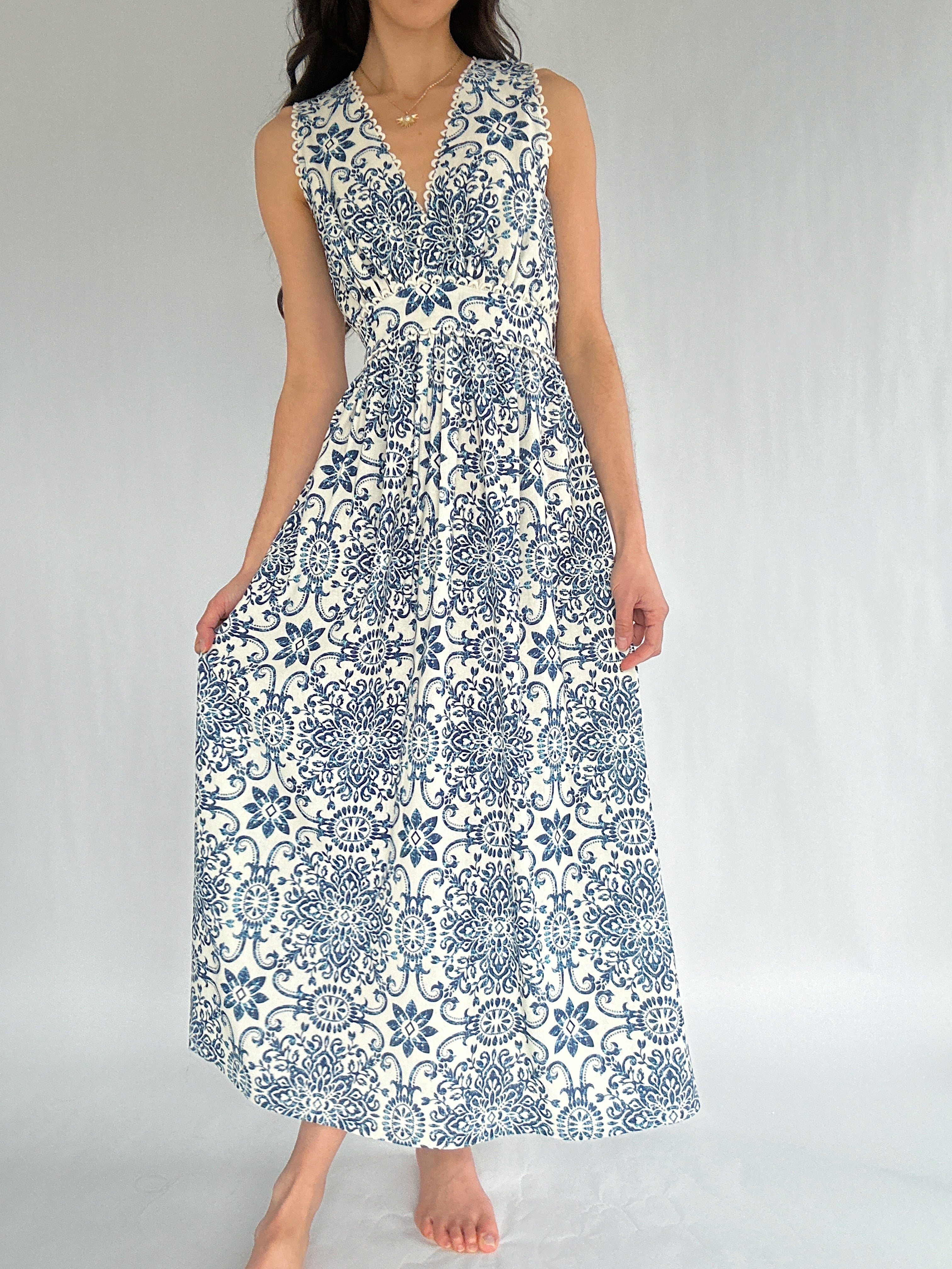 Woman wearing a sleeveless dress with blue floral pattern on a plain background