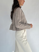Person wearing a brown peplum cardigan top and white pants against a plain background showing side