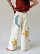 Person wearing white pants with star and moon patches on the back against a plain background