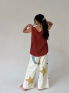 Person wearing a rust-colored sleeveless top and white pants with star patterns on a plain background from back