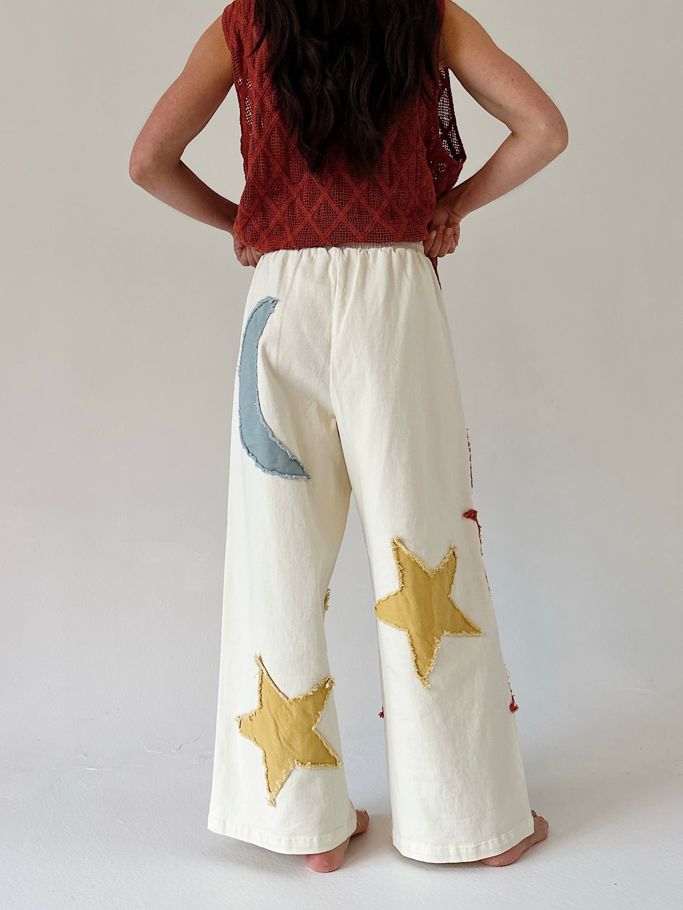 Person wearing white pants with star and moon designs on a plain background