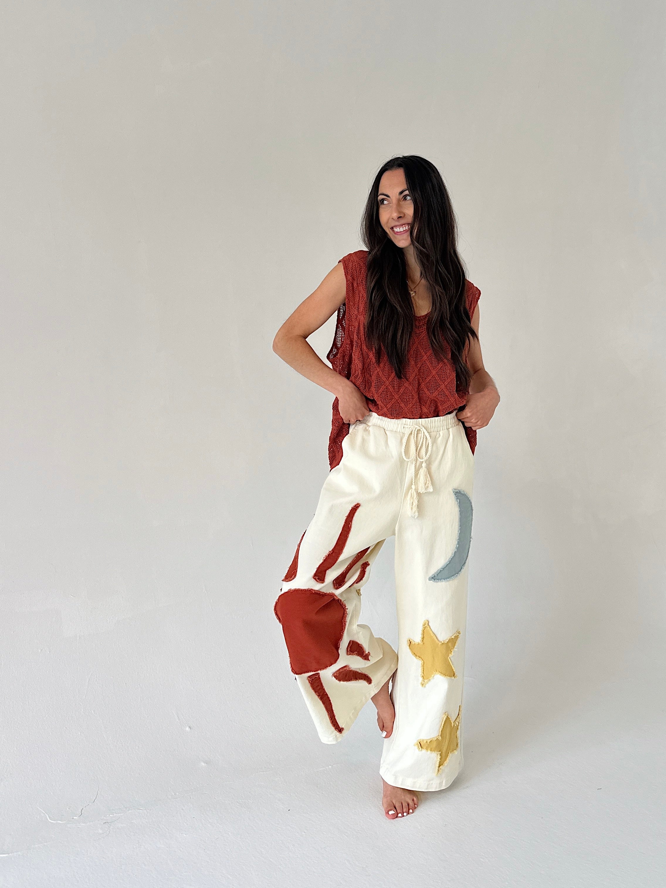 Woman wearing a rust-colored sleeveless top and white pants with star patterns on a plain background