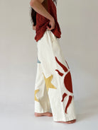 Person wearing white pants with red and gold abstract designs on a plain background
