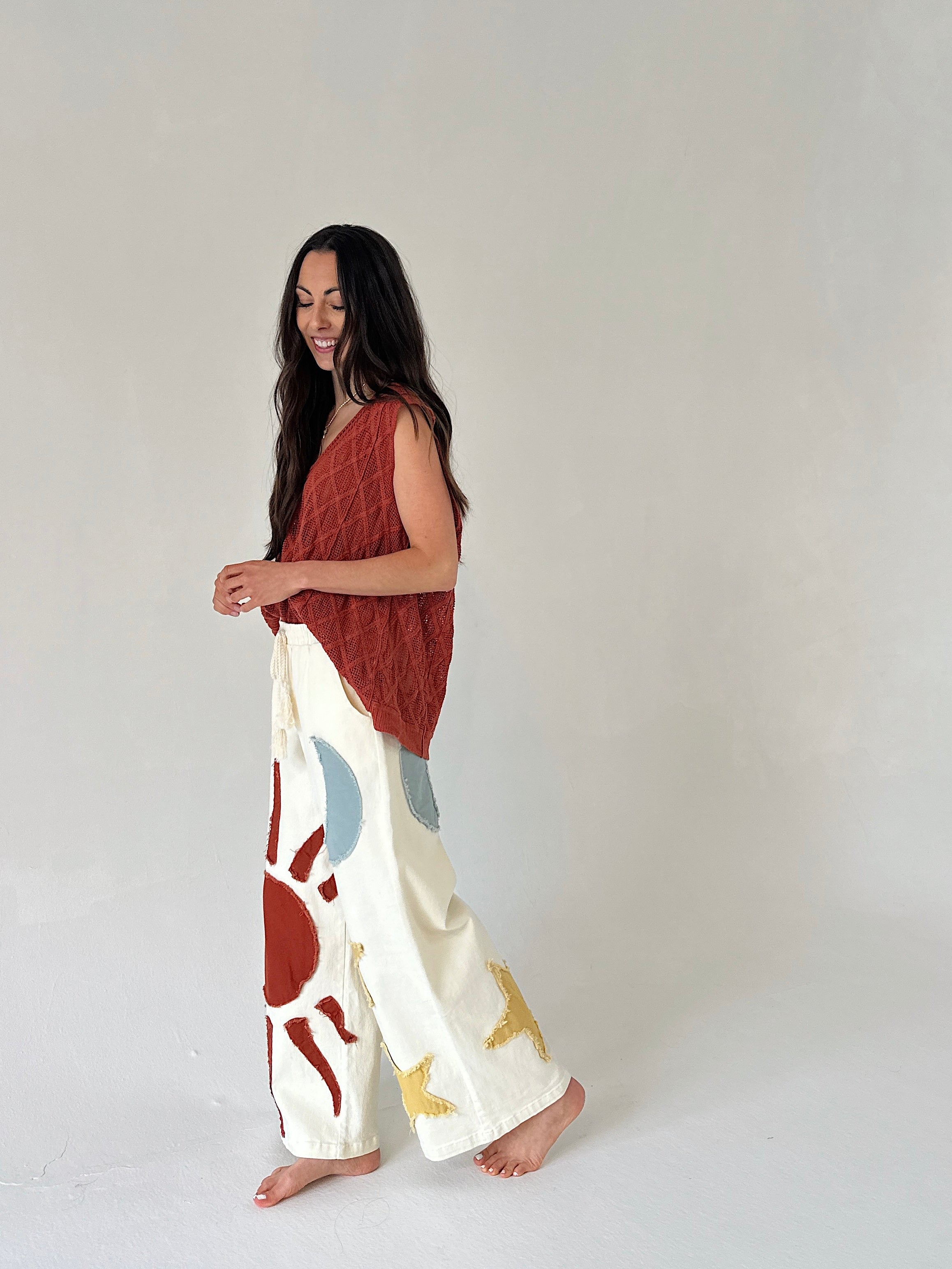 Woman wearing a rust-colored top and white pants with abstract patterns on a plain background