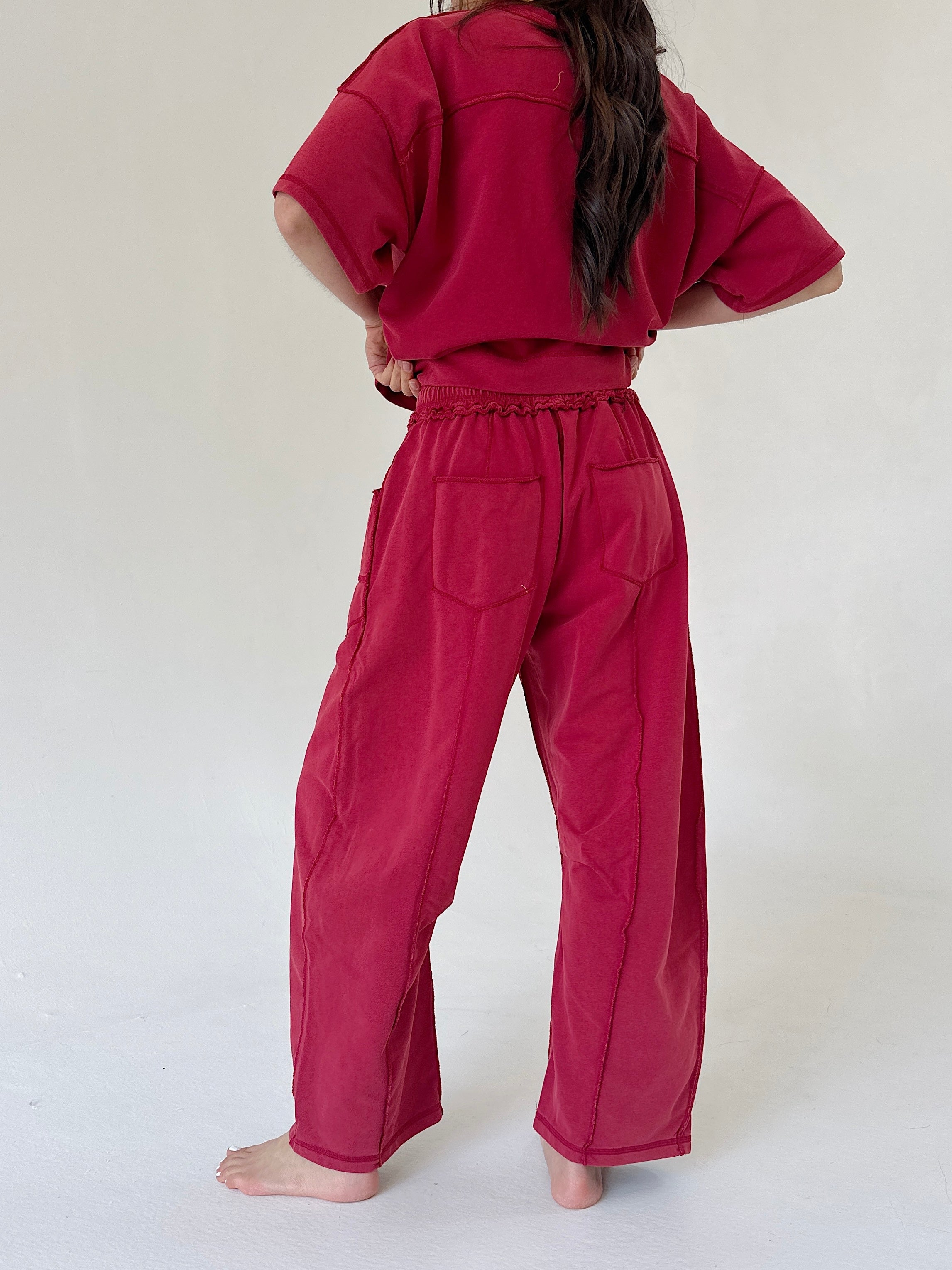 A person shown from the back wearing a matching deep red cropped short-sleeve top and wide-leg pants with large patch pockets, standing barefoot against a plain light background.