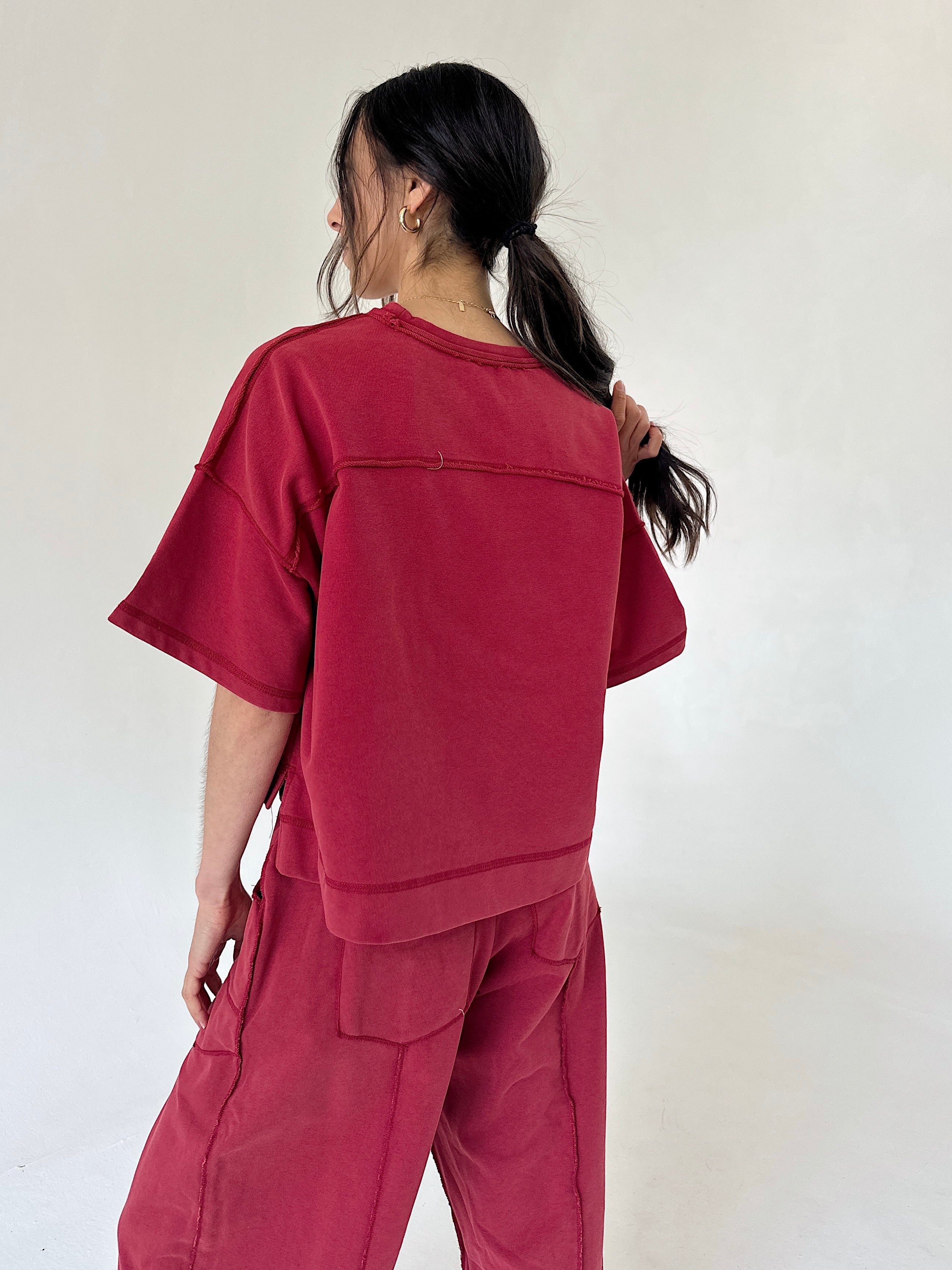 A model shown from the back wearing a matching red two-piece outfit consisting of a short-sleeve cropped top and wide-leg cargo pants, set against a plain off-white background.