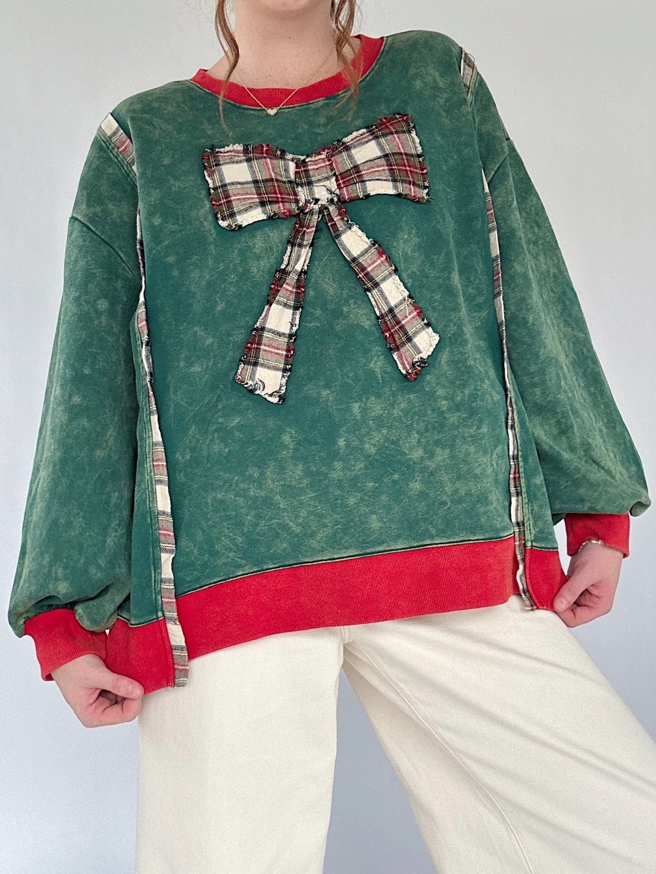 Green pullover with a plaid bow and red trim worn by a person on a white background