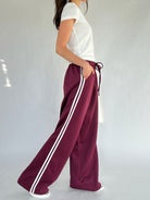 Person wearing maroon pants with white stripes on a plain background