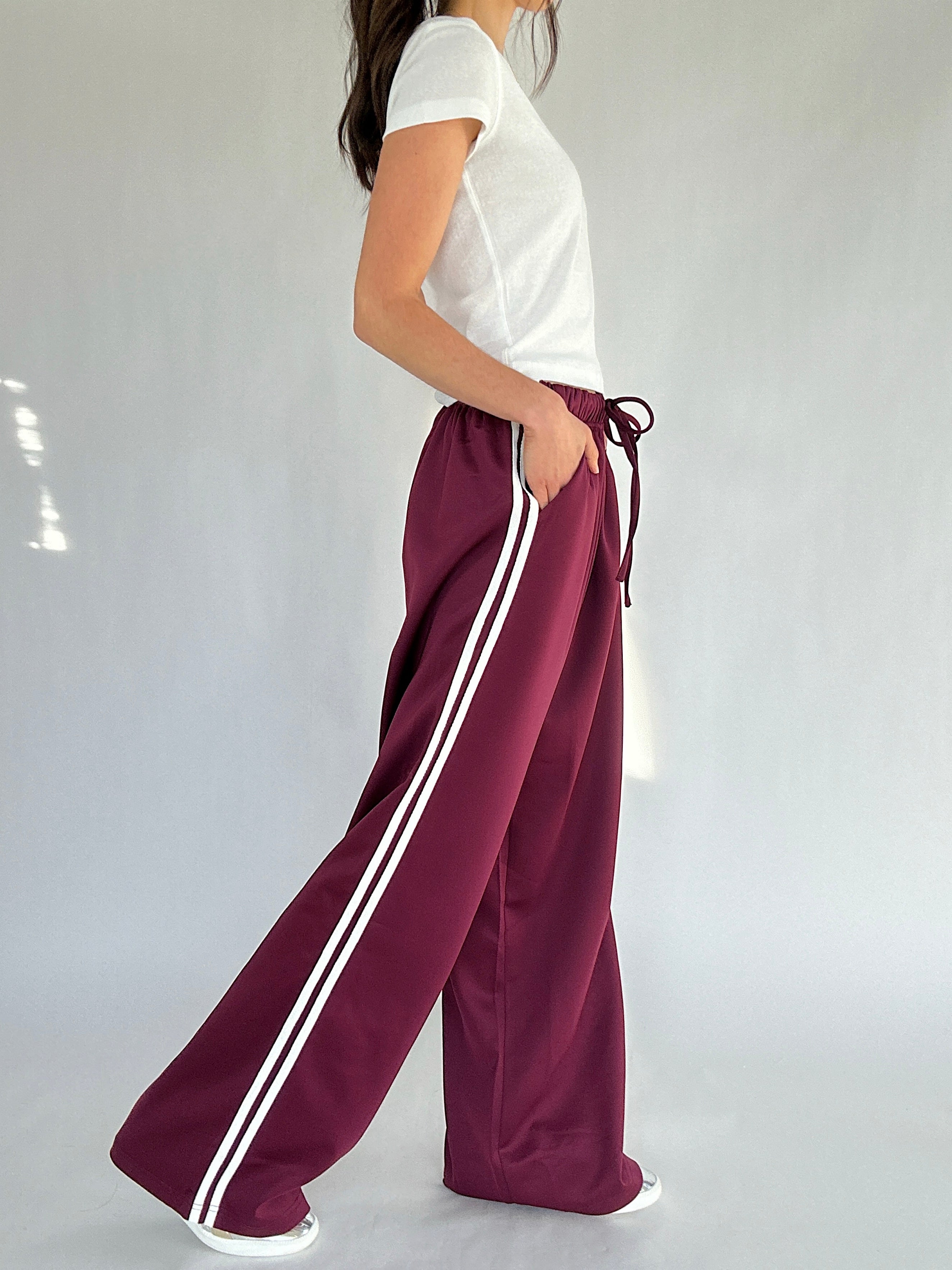 Person wearing maroon pants with white stripes on a plain background