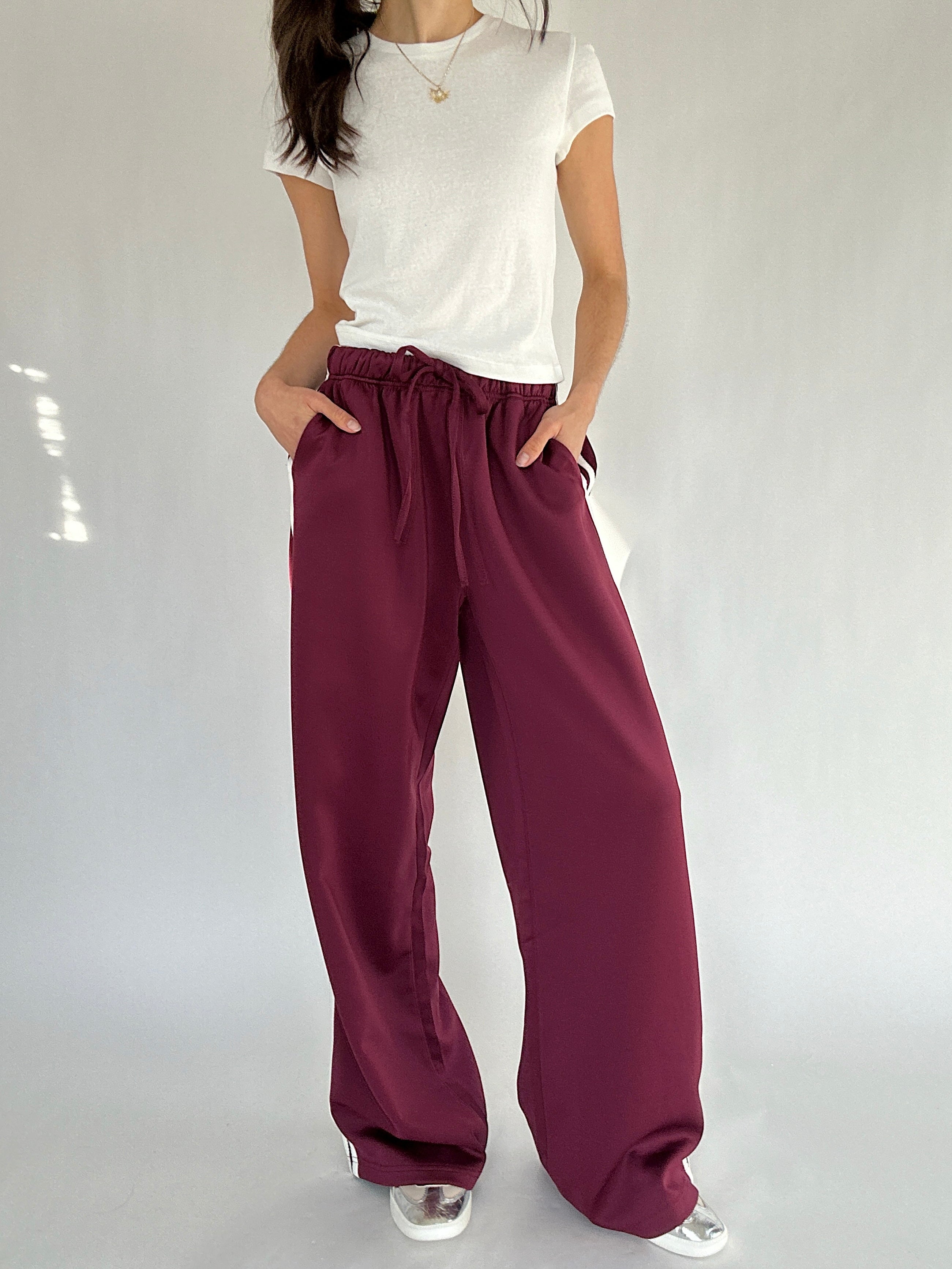 Person wearing a white top and maroon pants on a plain background