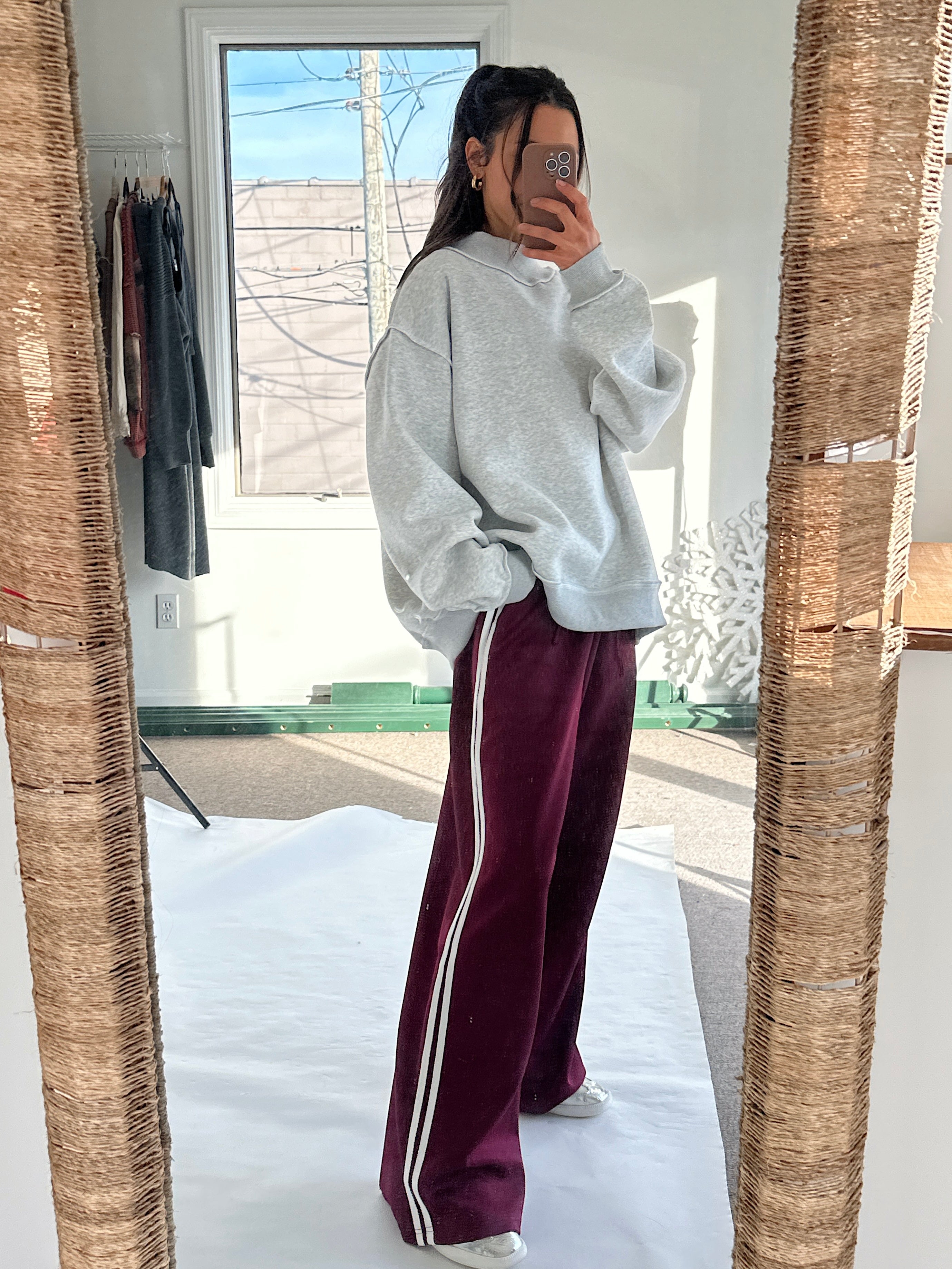 Person wearing a gray sweatshirt and maroon tracksuit with white stripes in a mirror