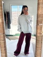 Person wearing a gray sweatshirt and maroon pants taking a mirror selfie.