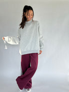 Woman wearing a gray sweatshirt and burgundy pants on a white background