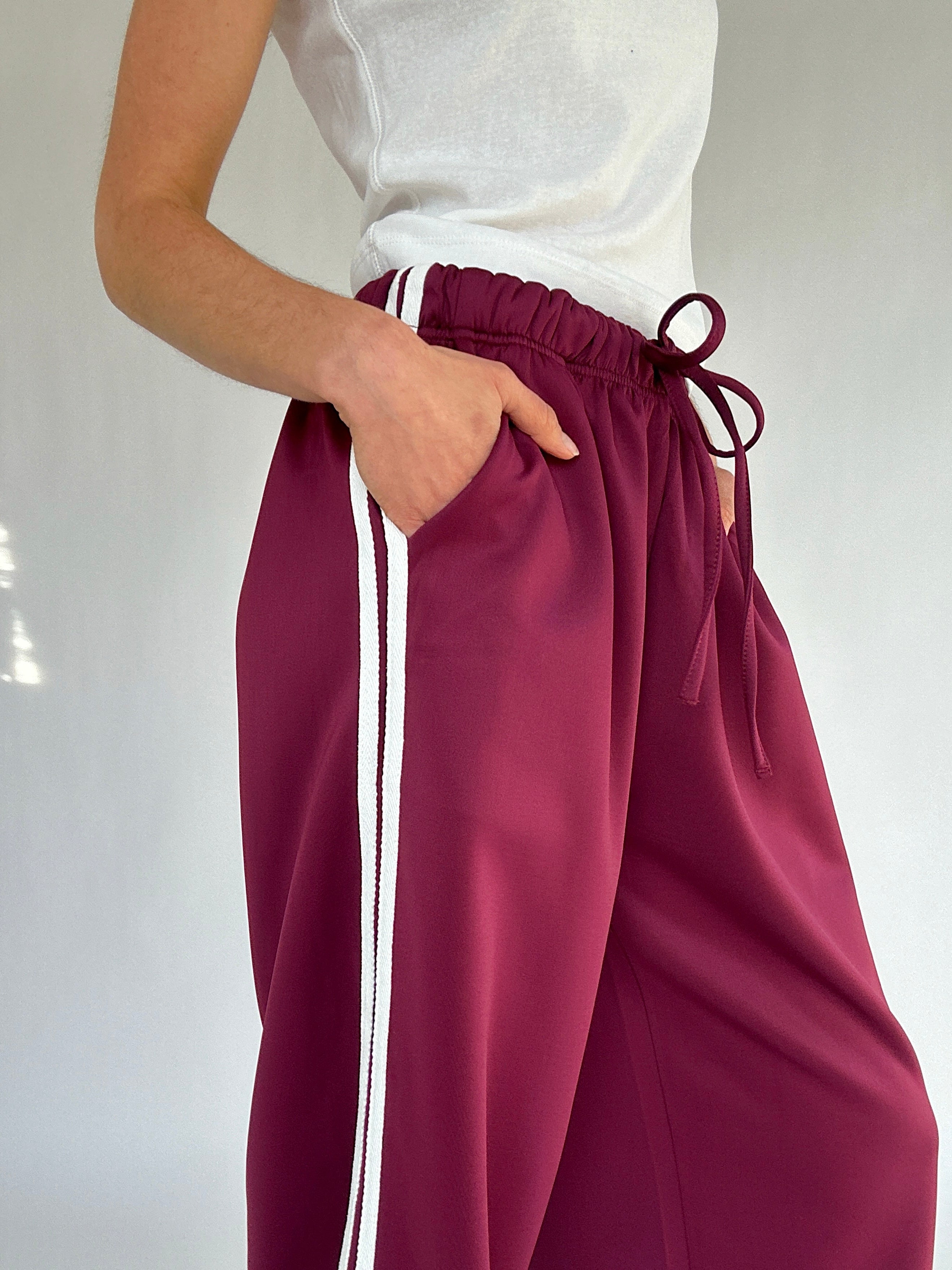 Maroon pants with white stripes worn by a person on a plain background
