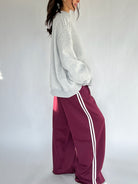 Person wearing a gray sweatshirt and maroon track pants with white stripes on a white background