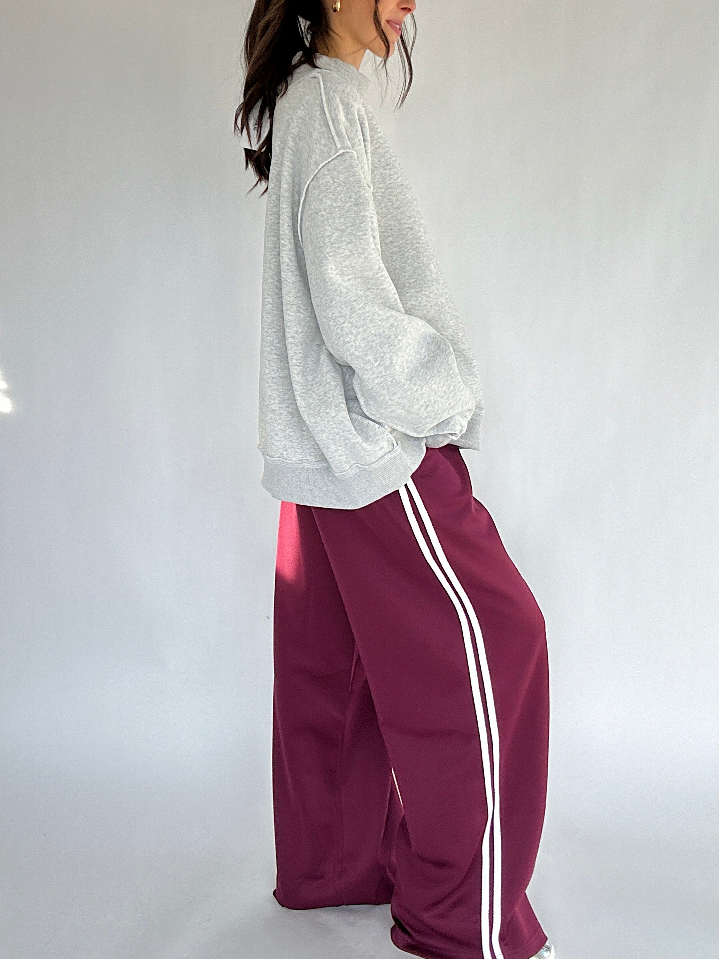 Person wearing a gray sweatshirt and maroon track pants with white stripes on a white background