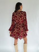 Woman wearing a red floral lace dress with beige knee-high boots on a white background
