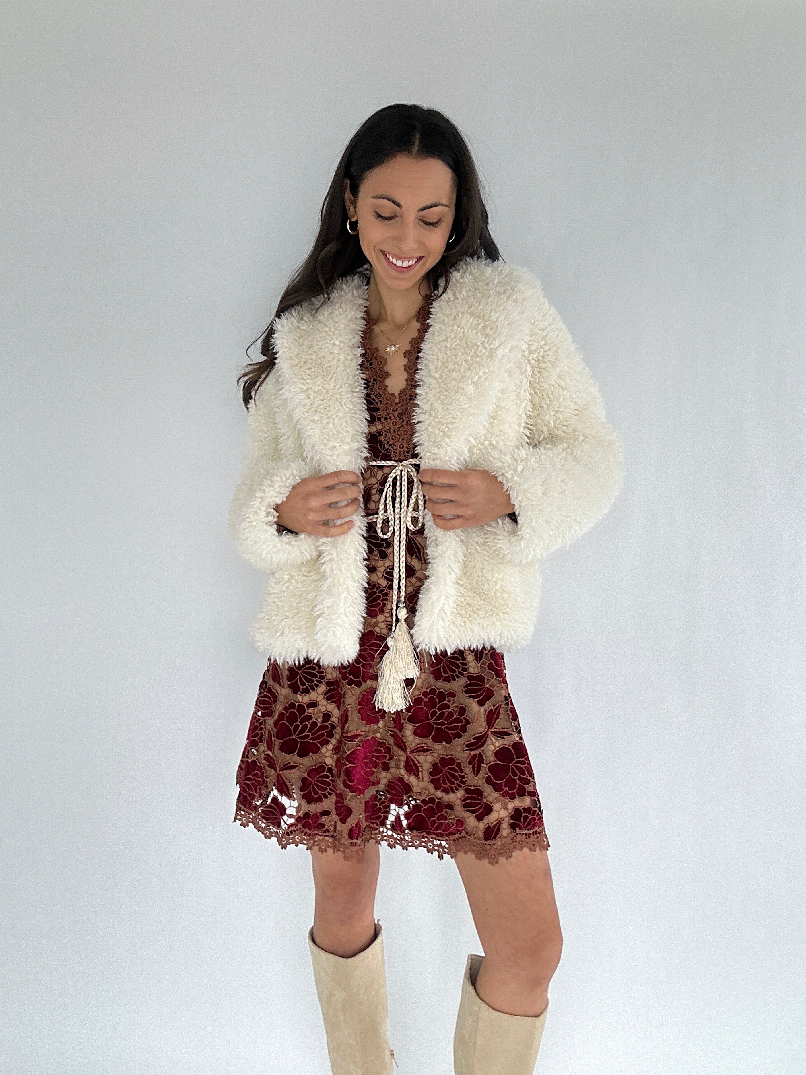 Woman wearing a white fluffy cardigan over a patterned dress on a plain background
