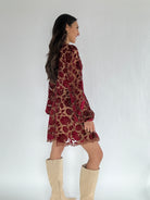 Woman wearing a red floral velvet burnout dress with beige knee-high boots on a white background