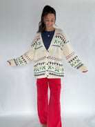 Woman wearing a patterned knit cardigan and red pants on a white background