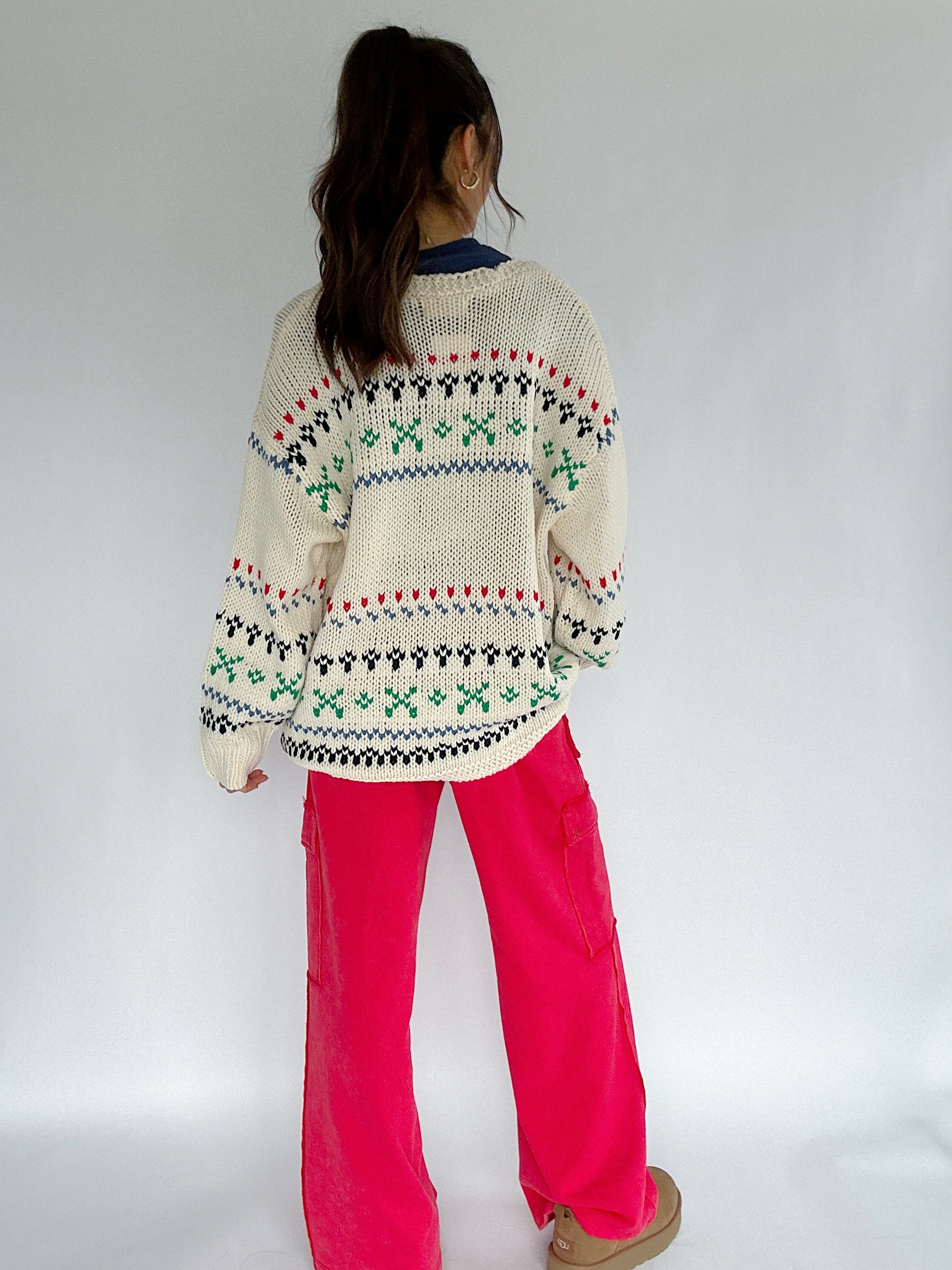 Person wearing a patterned sweater and pink pants on a white background